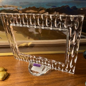 May include: A clear glass picture frame with a textured design. The frame has a stand and a Marquis label.