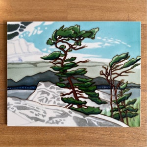 Puede incluir: Un azulejo de cerámica con una escena pintada de dos pinos en un acantilado rocoso con vistas a una masa de agua. El cielo es azul con nubes blancas y los árboles son verdes con troncos marrones. El azulejo es blanco con una superficie texturizada.