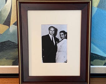 May include: A framed black and white photograph of a man and a woman. The frame is dark brown with a gold inner border. The photograph is centered within a cream-colored mat.