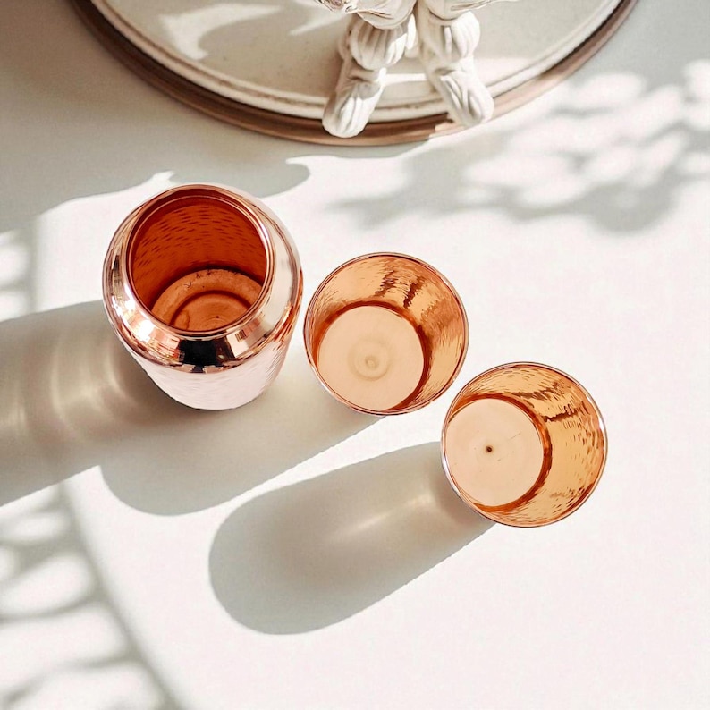 Pu&ograve; includere: Tre portacandele color rame con una texture martellata. Uno &egrave; a forma di vaso rotondo pi&ugrave; grande, e gli altri due sono tazze pi&ugrave; piccole a cielo aperto. I portacandele sono disposti su una superficie bianca, con ombre.