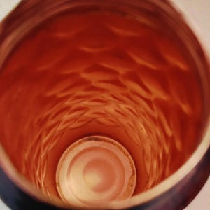 May include: An inside view of a cylindrical container with a textured, diamond-like pattern. The interior is a warm orange color, with a lighter, circular base. The container's rim is a darker shade, creating a contrast.