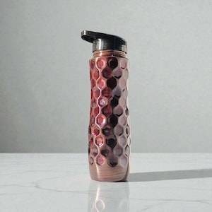 May include: A copper-colored water bottle with a textured, honeycomb-like pattern. The bottle has a black flip-top lid and a metallic finish. The design features shades of red and brown, creating a visually appealing and functional item.