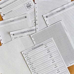 May include: A selection of white paper planner inserts with different layouts, such as lined notes, project lists, and a grid. Some pages have floral accents and the words "Ideas/Tutorials/Techniques" and "Commissions."