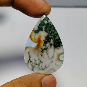 May include: A teardrop-shaped moss agate gemstone. The stone features a mix of colors, including green, white, orange, and light blue. The green areas resemble a forest, while the other colors create a unique pattern.