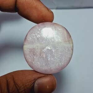 Op de afbeelding: Een ronde, witte, iriserende edelsteen met een lichtroze tint. De edelsteen heeft een glad, gepolijst oppervlak en een natuurlijk, organisch patroon.