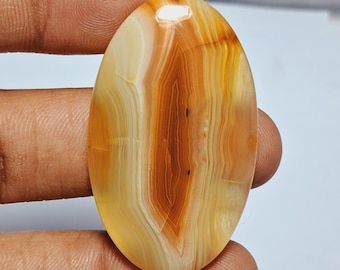 May include: Oval shaped agate cabochon with a mix of white, yellow, and orange banding. The stone has a smooth, polished surface.