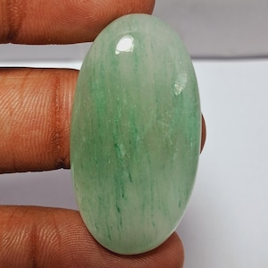 May include: Oval shaped green and white agate cabochon with a polished finish. The stone has a translucent appearance with green streaks throughout.