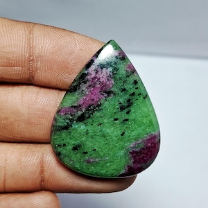 May include: A polished, teardrop-shaped gemstone featuring a vibrant green base color with striking inclusions of deep magenta and black. The stone's surface is smooth and reflective, showcasing a natural, organic pattern. This gemstone is ideal for jewelry making.