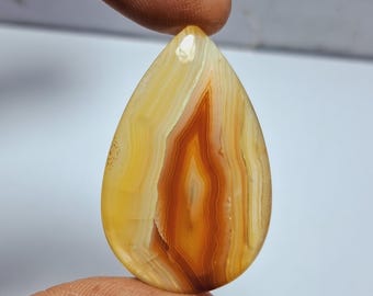 May include: A teardrop-shaped agate cabochon with a yellow, orange, and white banded pattern.
