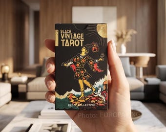 May include: A rectangular deck of Black Vintage Tarot cards featuring a black box with gold and red illustrations. The front displays a figure standing on a rocky cliff with a dog, a sun, and the text Black Vintage Tarot and Regin Collective.
