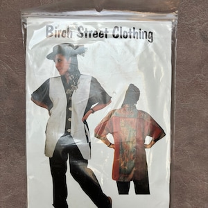 May include: A sealed plastic package featuring a clothing pattern. The package displays a woman wearing a white vest and black pants, and a colorful jacket. Text on the package reads "Birch Street Clothing" and "Dee-lightful Jacket & Pants XS-XXL."