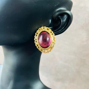 May include: A pair of gold tone earrings with a pink oval cabochon stone set in a filigree design.