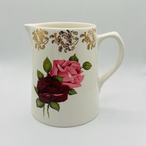 May include: White ceramic pitcher with a gold floral design and two roses, one pink and one red.