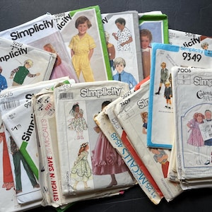 May include: A collection of vintage sewing patterns from brands like Simplicity and McCall's. The patterns feature illustrations of children's clothing, including dresses, suits, and pajamas. The patterns are in various sizes and colors.
