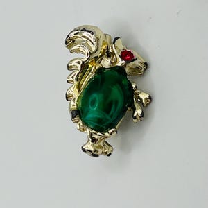 May include: A gold-toned brooch featuring a squirrel with a green gemstone and a red rhinestone eye.