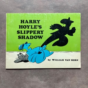 May include: A green book cover with the title "HARRY HOYLE'S SLIPPERY SHADOW" in black text. The cover features an illustration of a man in a blue outfit with a cat, and his shadow running away from him.