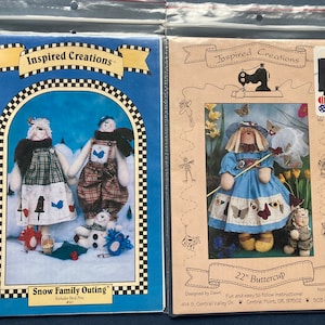 May include: Two craft pattern packets in plastic sleeves. One features a snowman family outing with the text "Snow Family Outing". The other shows a doll in a blue dress with the text "22" Buttercup". Both packets are from "Inspired Creations".