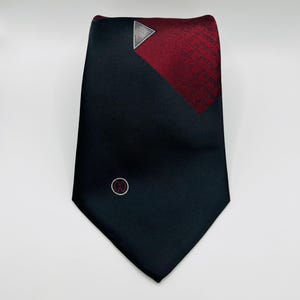 May include: A black and red patterned tie with a white triangle and a small circle logo in the center.