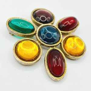 May include: A vintage brooch featuring seven colorful, oval-shaped cabochon stones in shades of green, red, yellow, and blue, set in a gold-toned metal frame. The brooch has a flower-like arrangement, with each stone surrounded by a textured border.