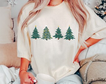 May include: A cream-coloured t-shirt with a graphic of four green Christmas trees with yellow stars and colourful lights.