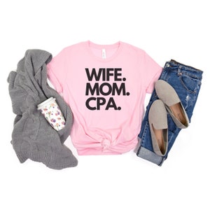 Könnte beinhalten: Rosa T-Shirt mit dem Text "WIFE. MOM. CPA." in schwarzen Buchstaben.