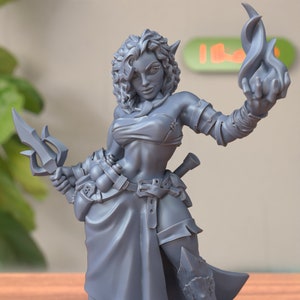 Peut inclure: Une figurine d'elfe guerrière féminine en gris, imprimée en 3D, tenant une lance et une flamme dans l'autre main. Elle porte une jupe en cuir et un haut avec une ceinture.