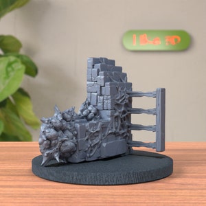 May include: A gray 3D printed miniature of a ruined stone wall with vines and a wooden fence. The miniature is on a black base.