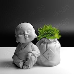 May include: A white ceramic figurine of a meditating Buddha with a small plant in a white ceramic pot shaped like a bag. The plant has green leaves.