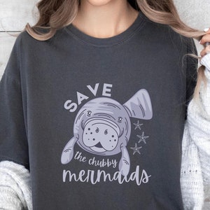 May include: A dark gray t-shirt with a graphic of a manatee and the text "SAVE the chubby mermaids".