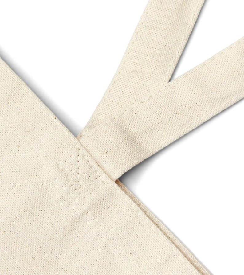 May include: Close-up of the top of a beige canvas tote bag with a reinforced seam at the top of the handle.