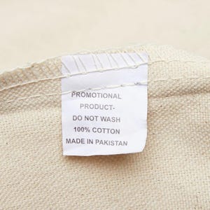 May include: White fabric tag with black text that reads "Promotional Product - Do Not Wash 100% Cotton Made in Pakistan".