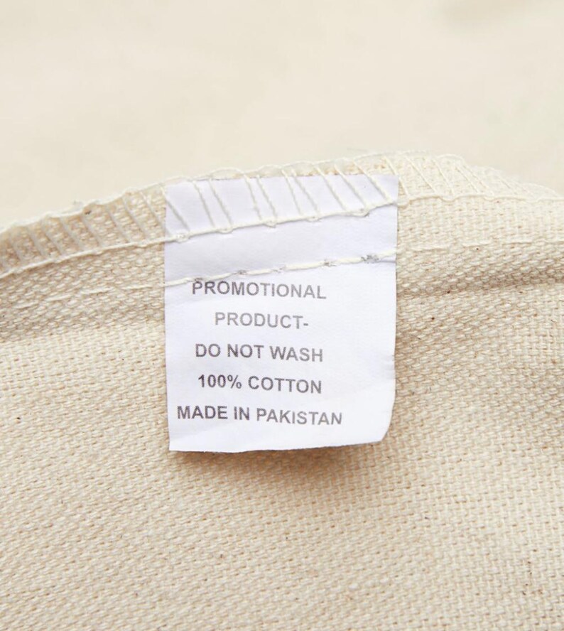 May include: White fabric tag with black text that reads "Promotional Product - Do Not Wash 100% Cotton Made in Pakistan".