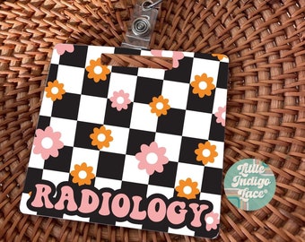 May include: A pink and orange floral patterned badge holder with the word "RADIOLOGY" in pink letters. The badge holder has a black and white checkered background and is attached to a retractable badge reel.