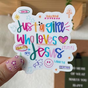 May include: A white sticker with the text "Just a girl who loves Jesus" in colorful lettering. The sticker includes additional text and small illustrations, such as a heart, cross, and stars.