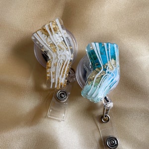 Pu&ograve; includere: Due porta badge in plastica trasparente con un design di osso anatomico in oro e bianco. Un porta badge ha uno sfondo bianco con brillantini dorati e l'altro ha uno sfondo blu con brillantini dorati.