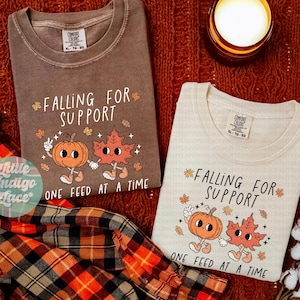 May include: Two t-shirts with the text "FALLING FOR SUPPORT" and a cartoon pumpkin and leaf design. One shirt is brown, the other is cream. A plaid shirt and a lit candle are also in the image. The word "espresso" is at the bottom.