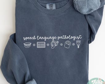 May include: A dark blue sweatshirt with the text "speech language pathologist" and a row of icons including a mouth, calendar, ear, brain, and a flower.