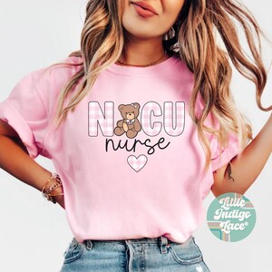 Puede incluir: Camiseta rosa con un patr&oacute;n de cuadros rosa y blanco. La camiseta tiene un gr&aacute;fico de un osito de peluche con un lazo y el texto "NICU nurse" con un coraz&oacute;n rosa.