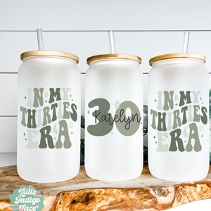 May include: Three frosted glass tumblers with bamboo lids and straws. The tumblers have a white background with green text and graphics. The text on the tumblers reads "In My Thirties Era" and "Katelyn 30".