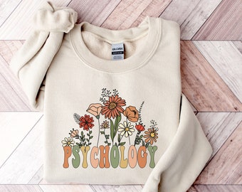 May include: A beige sweatshirt with a floral design and the word "PSYCHOLOGY" in green, orange, and yellow letters.