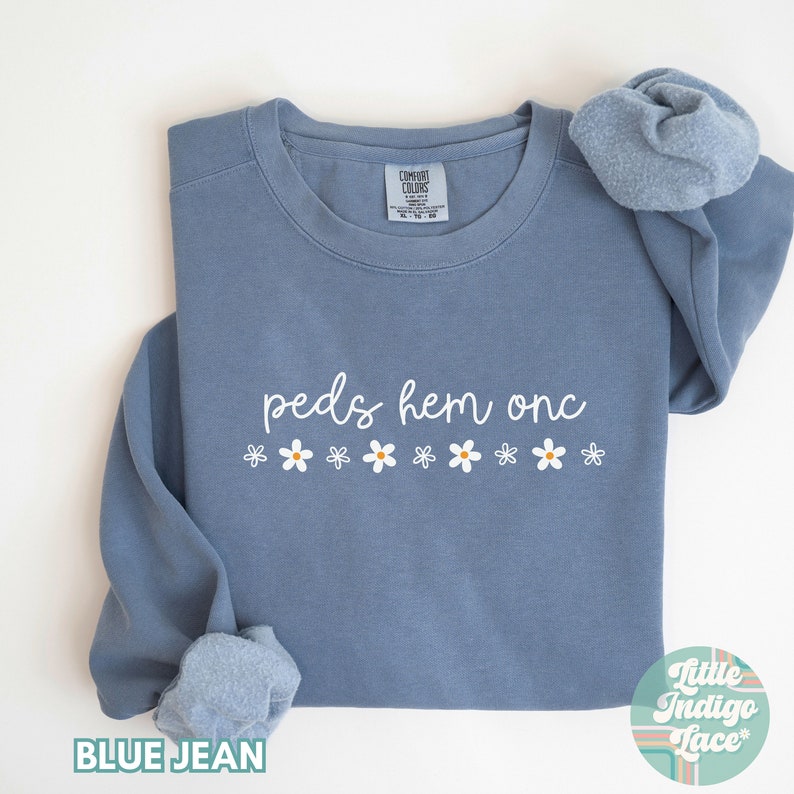 May include: A blue jean sweatshirt with the text "peds hem onc" and a row of white daisies.