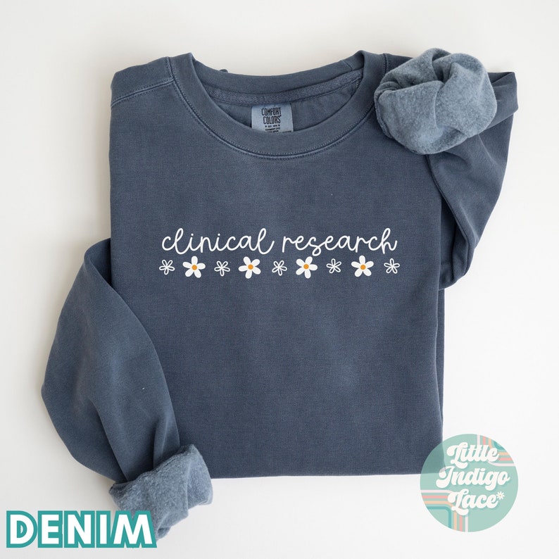 May include: A denim blue sweatshirt with the text "clinical research" in white lettering and a row of white daisies with yellow centers.