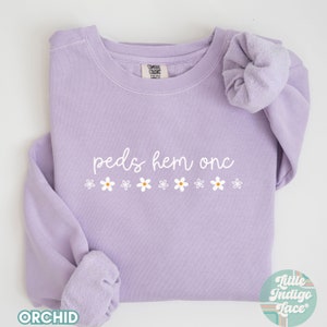 May include: A lavender sweatshirt with the text "peds hem onc" and a row of white daisy flowers printed on the front.