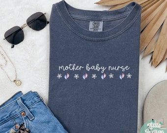 May include: A dark blue t-shirt with the text "mother baby nurse" in white lettering. The shirt has a small pink and blue footprint design with white flowers on either side of the text.