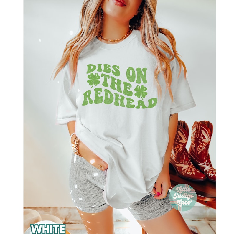 Op de afbeelding: Wit T-shirt met groene klavergraphics en de tekst "DIBS ON THE REDHEAD".