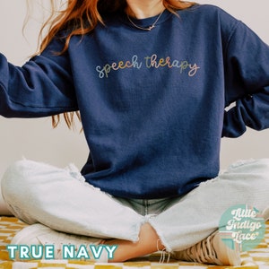 May include: A navy blue sweatshirt with the text "speech therapy" written in colorful script.