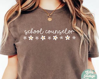 May include: A brown t-shirt with the text "school counselor" in white lettering. The text is surrounded by a row of white daisies.