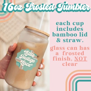 May include: A 16 ounce frosted glass tumbler with a bamboo lid and straw. The tumbler is filled with a light brown beverage and has a sticker that says "Little Indigo Lace*" on it.