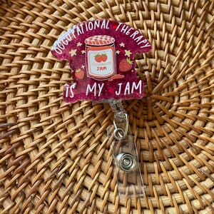 Puede incluir: Un portagafete de purpurina rosa con un tarro de mermelada de fresa y el texto "Occupational Therapy is my jam".