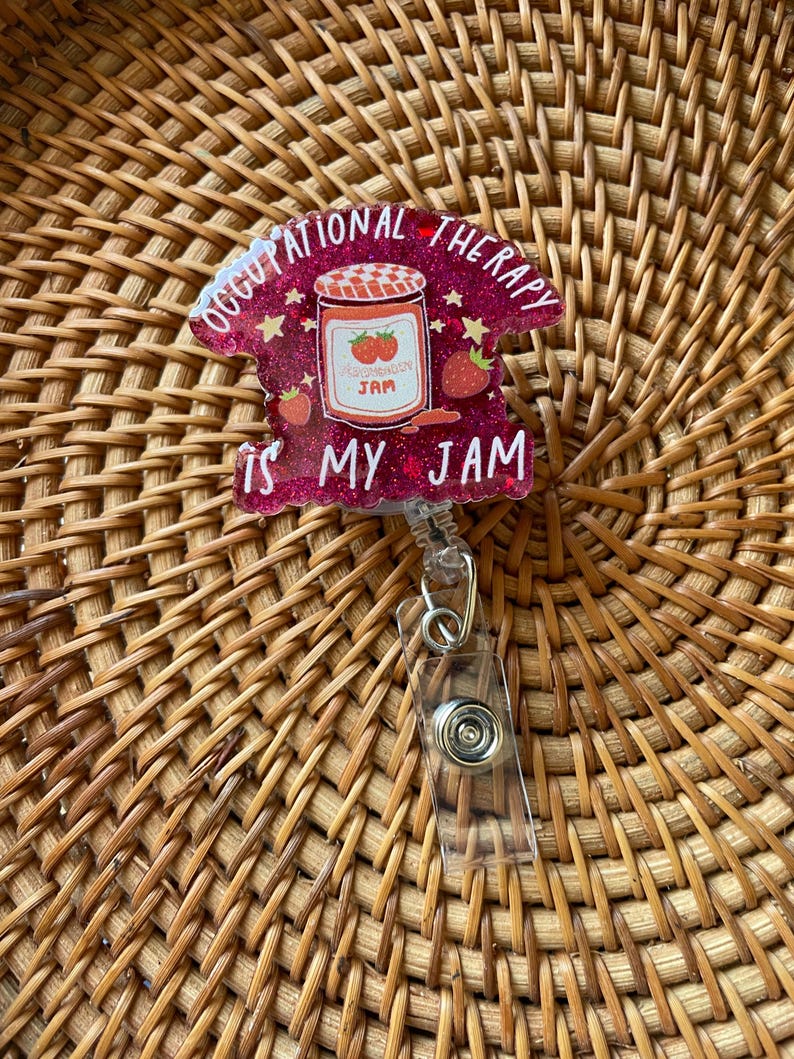Puede incluir: Un portagafete de purpurina rosa con un tarro de mermelada de fresa y el texto "Occupational Therapy is my jam".